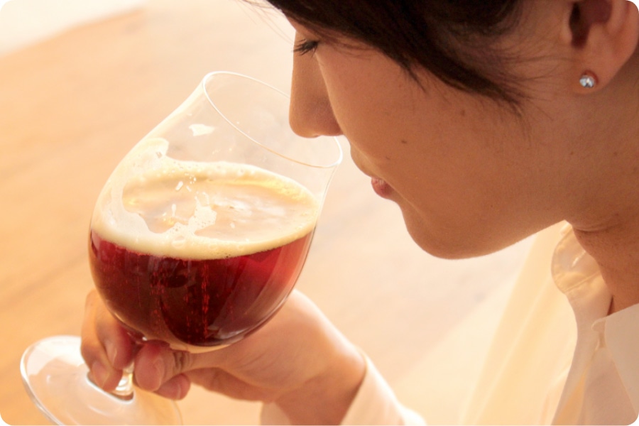 グラスに鼻を近づけ、クラフトビールの香りを楽しんでいる女性の画像