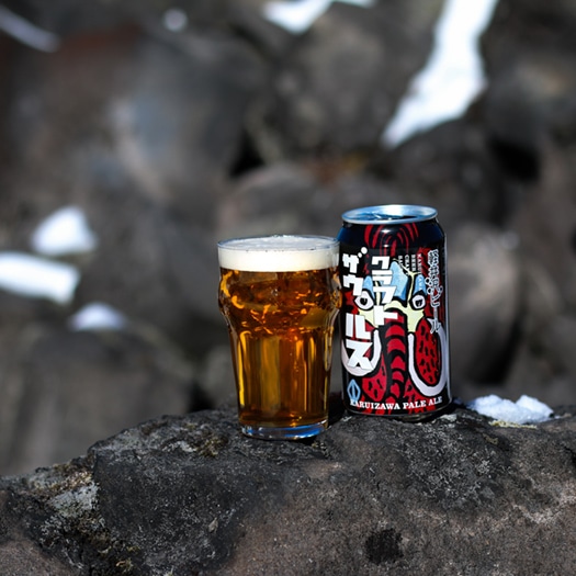 岩場に、軽井沢ビールクラフトザウルスペールエールの缶とビールが注がれたグラスが並ぶ画像