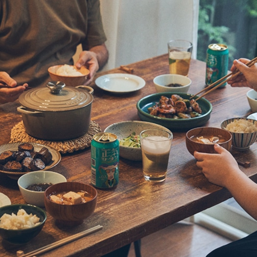 テーブルの上においしそうな料理とグラスに注がれた正気のサタンが並び、人が向かい合ってご飯をたべている画像