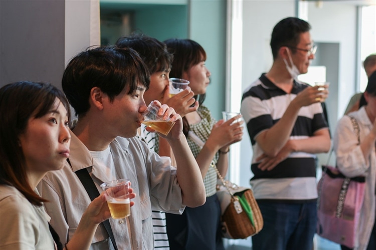 複数の参加者がモニターの解説を見ながらクラフトビールを飲んでいる画像