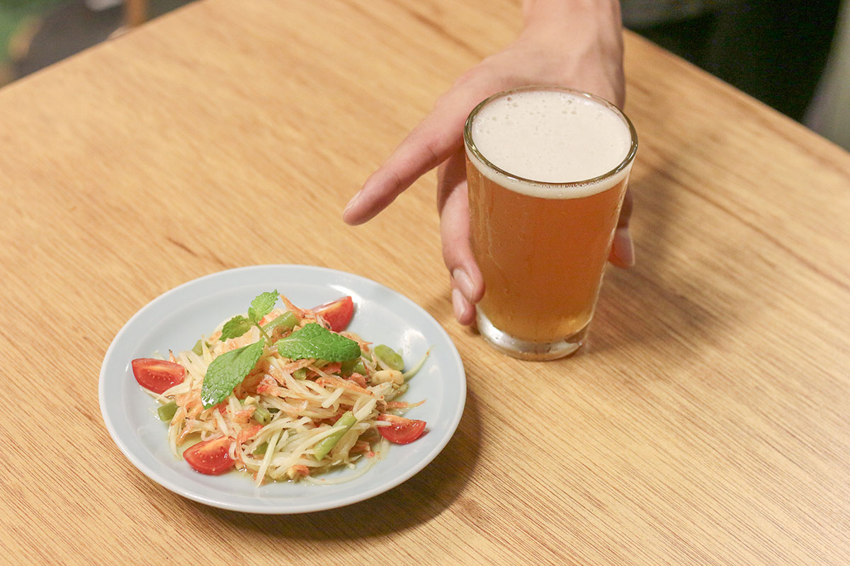 麦酒宿 まり花 道玄坂のフード「青パパイヤサラダ」と福井県のアワーブルーイングのサワーIPA「アワータイム」がテーブルの上に並んでいる画像