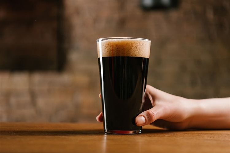グラスに注がれた黒ビールをテーブルの上に手を添えて置いている画像