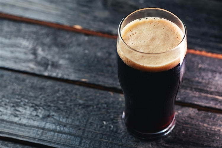 グラスに注がれた黒ビールが木目調のテーブルの上に置かれている画像