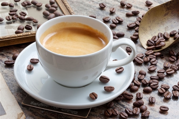 コーヒーカップに入ったカフェラテの周りにコーヒー豆がちりばめられている様子