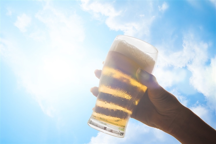 グラスに注がれたビールを青空に掲げている画像