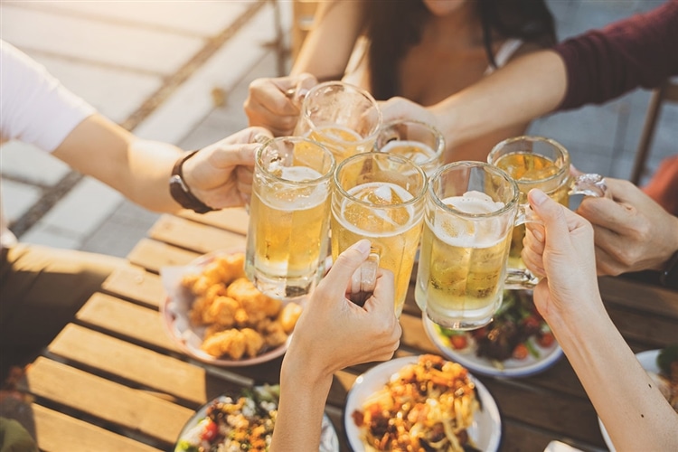 夏の昼間に、男女6人でジョッキに入ったビールで乾杯する様子を俯瞰で撮った画像