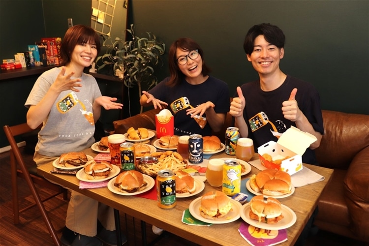 ハンバーガー13種類とクラフトビール、ポテトやナゲットなどがいっぱいのテーブルで楽しそうにしているヤッホーブルーイングの３人
