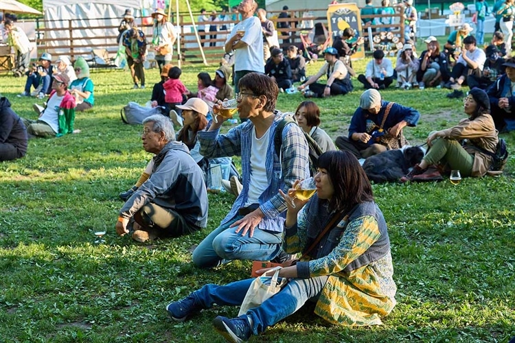 「よなよなエールの超宴2024 in 新緑の北軽井沢」で芝生の上に座ってステージライブを楽しんでいる参加者の様子