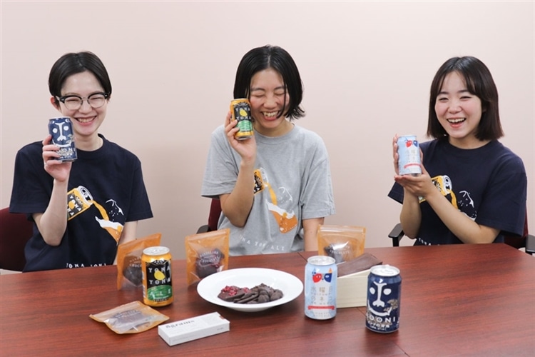 ヤッホーブルーイングの女性スタッフ3名がクラフトビールとチョコレートが並んだ机の前に座り、クラフトビールを手にもって笑っている様子