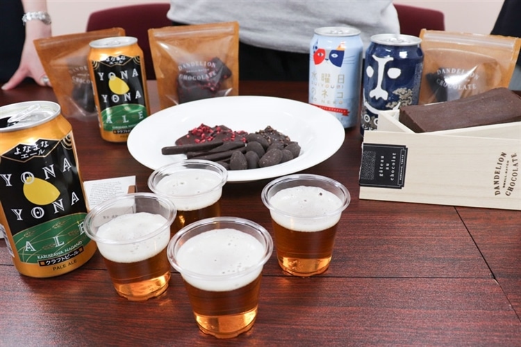 コップに入ったビールや、チョコレート、クラフトビールの缶が机の上に沢山載っている様子