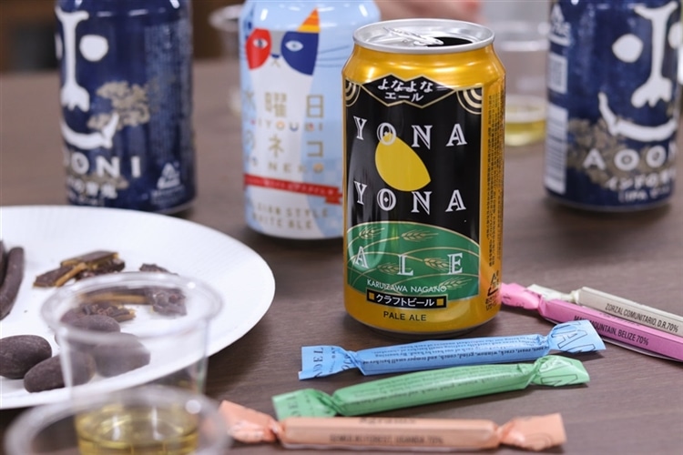 よなよなエール、インドの青鬼、水曜日のネコなどのクラフトビールの缶と、ダンデライオン・チョコレートの製品が机の上に並んでいる様子