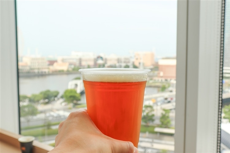 みなとみらいの景色を窓越しに見ながらプラカップに入ったクラフトビールを飲む様子