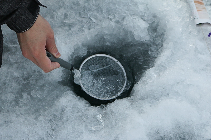 ワカサギ釣りの穴に溜まった氷をかきだしている様子
