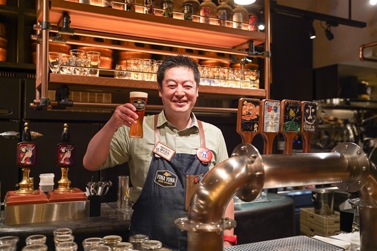YONA YONA BEER WORKS歌舞伎町店の支配人「ほくさん」が、ビールグラスを持って微笑んでいる様子