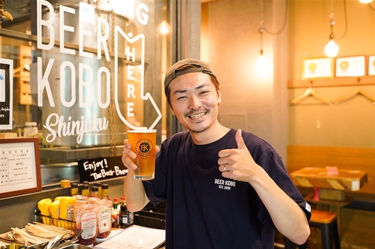 グラスに入ったクラフトビールを手に持った、笑顔のビール工房新宿店の男性スタッフの画像