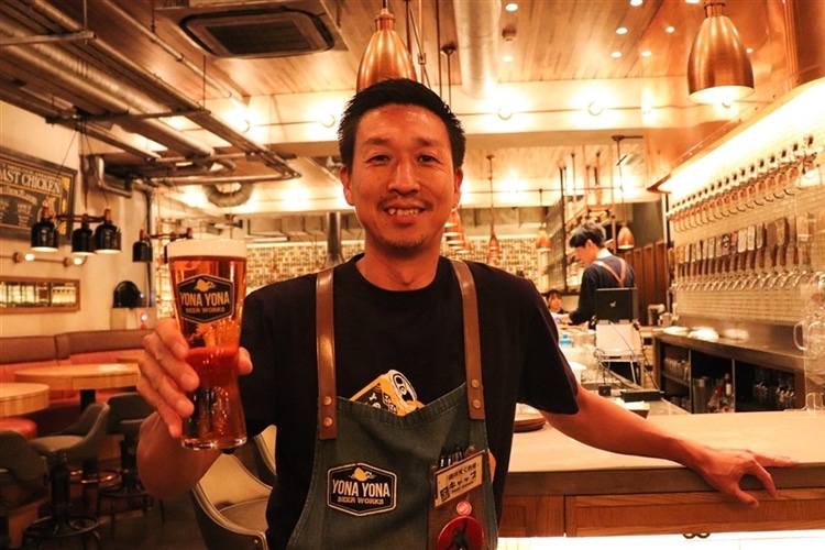 YONA YONA BEER WORKS新宿東口店の支配人「キャップ」が、ビールグラスを持って微笑んでいる様子
