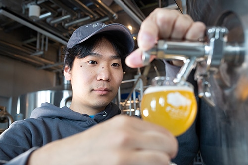 ブルワー(ビール醸造士)がタンクからグラスへビールを注いでいる画像