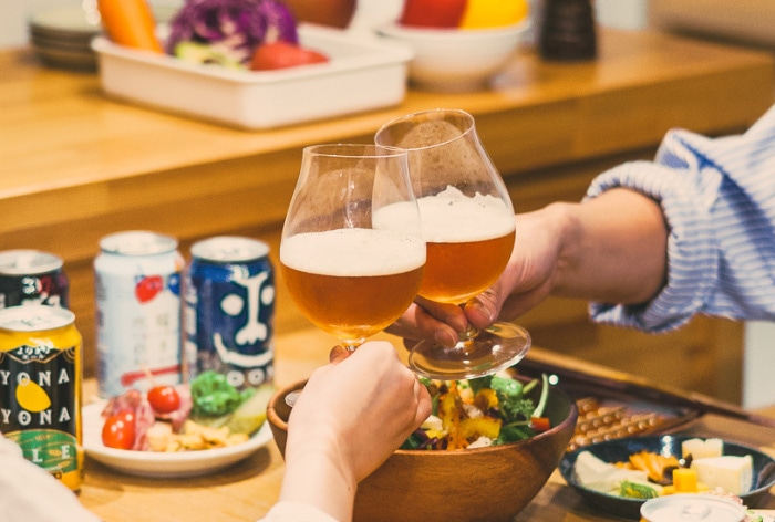 テーブルの上に食事が並び、クラフトビールで乾杯している画像