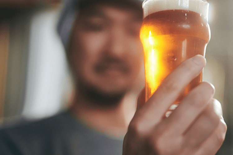 ブルワー（ビール醸造士）がよなよなエールを注いだグラスを持って眺めている画像
